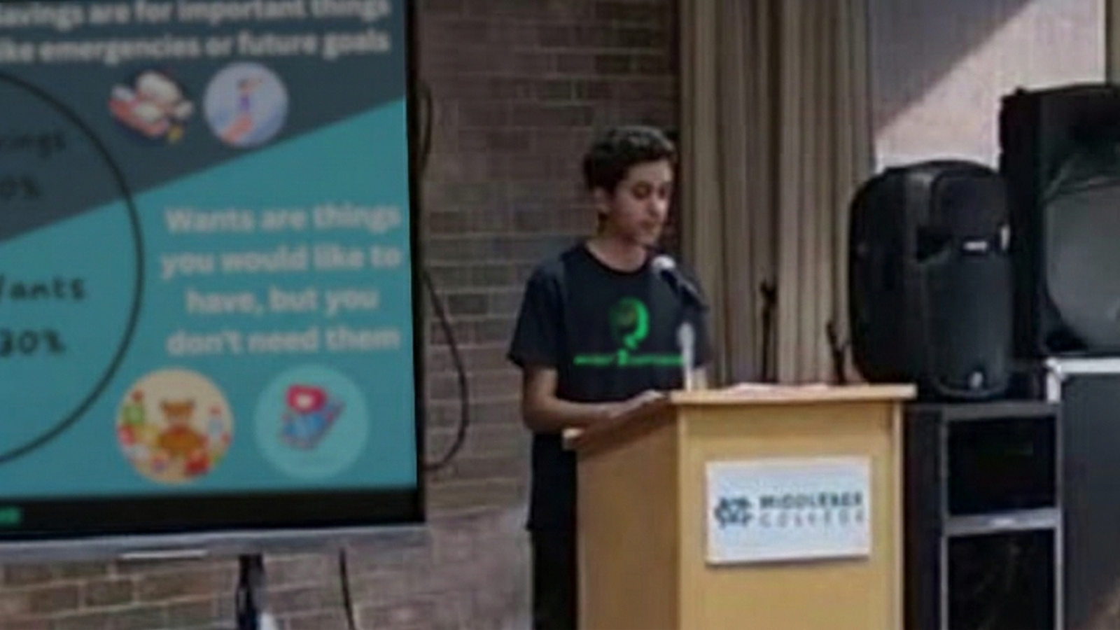 Aditya Herekar at a Middlesex College podium presenting a needs-versus-wants budgeting slide